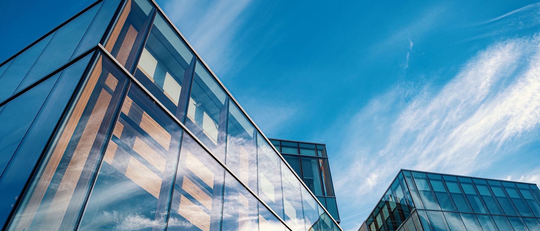 Sunlight on the glass and timber facade of a modern commercial building, looking up against a clear sky